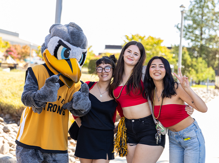 Three Butte College Students smile and pose with the mascot, Dash.